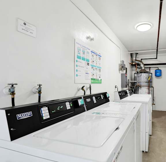 A clean, white industrial laundry room with Maytag washing machines and a white wall with a poster.
