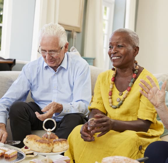 a group of older people sitting on a couch talking and eating food