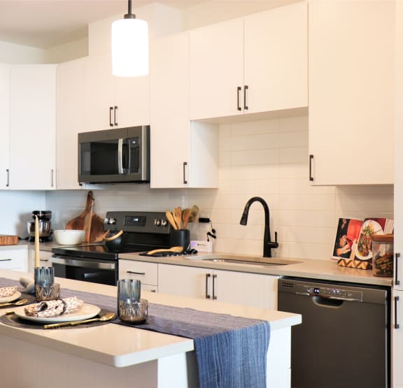 a kitchen with white cabinets and black appliances and a table with plates of food at Vyne One Loudoun, Ashburn, VA