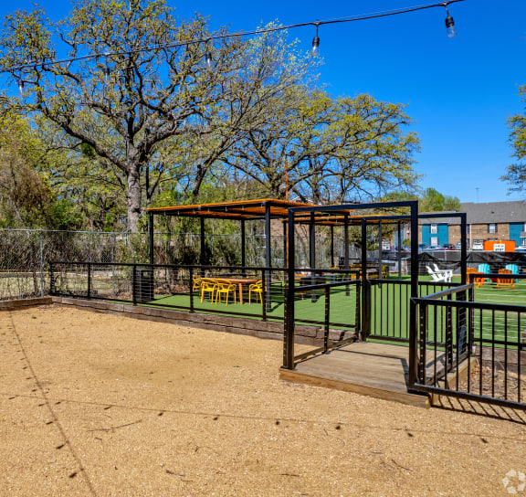 a fenced in dog park with a yellow bench and gazebo
