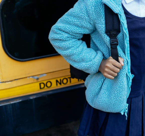 a woman wearing a blue sweater and a blue purse and a yellow bus