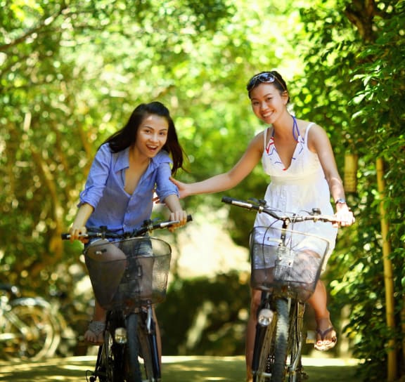 two women riding bikes down a path in the woods