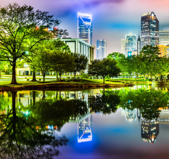 a city skyline at night reflected in a pond in a park