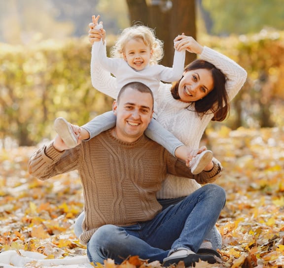 a father and mother holding their child in the autumn leaves