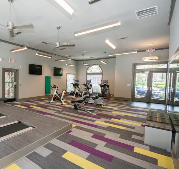 a gym with cardio machines and chairs in a building with glass doors