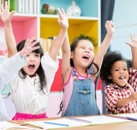 Four children are raising their hands in a classroom. at The Reserve at Sugarloaf Apartments, Duluth, GA, 30097