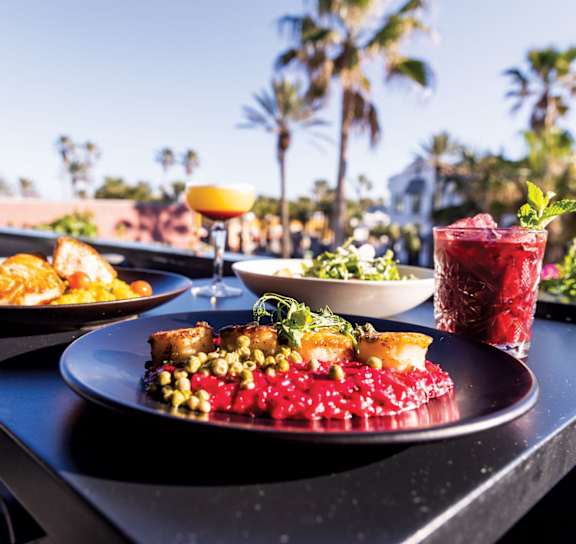 A table with food and drinks on it with a view of palm trees in the background.