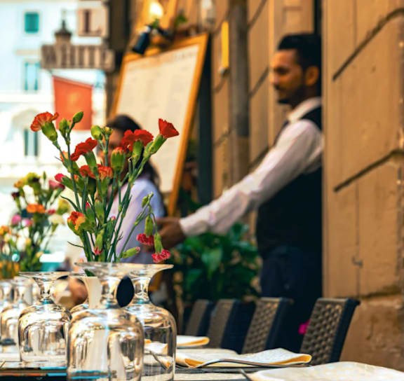 A waiter is setting a table with a vase of flowers in the foreground.