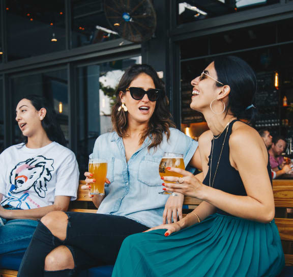 three women sitting on a bench with drinks