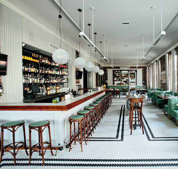 a long bar with green chairs and tables in a restaurant