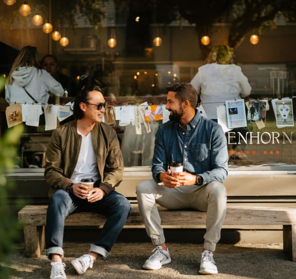 two men sitting on a bench in front of a store window