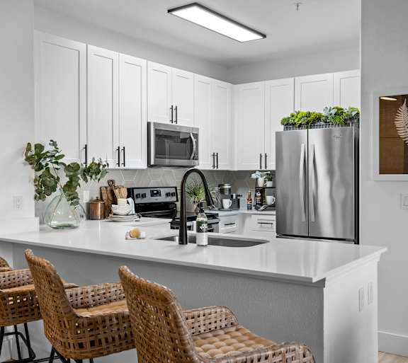 A kitchen with white cabinets and a white countertop with a refrigerator, microwave, and sink.