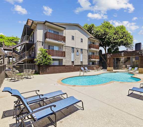 A pool surrounded by lounge chairs in front of apartment buildings.