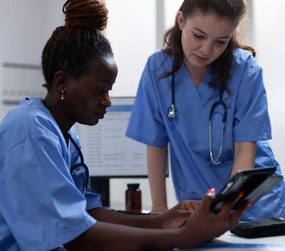 Two medical professionals in blue scrubs are reviewing a tablet.