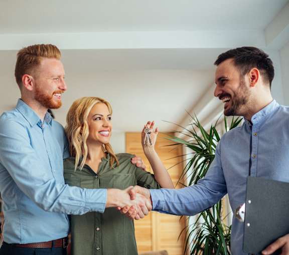 Two men shake hands with a woman in a room.