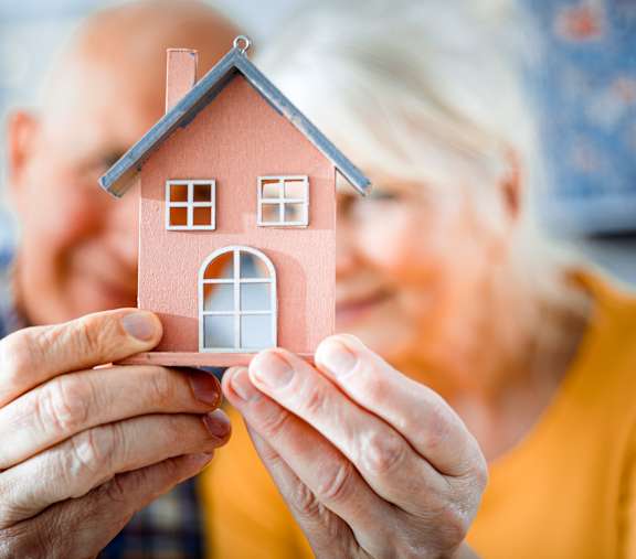 Elderly couple smiling and holding a small model house together at Humboldt Senior 55+ Apartments, Saint Paul, MN, 55107