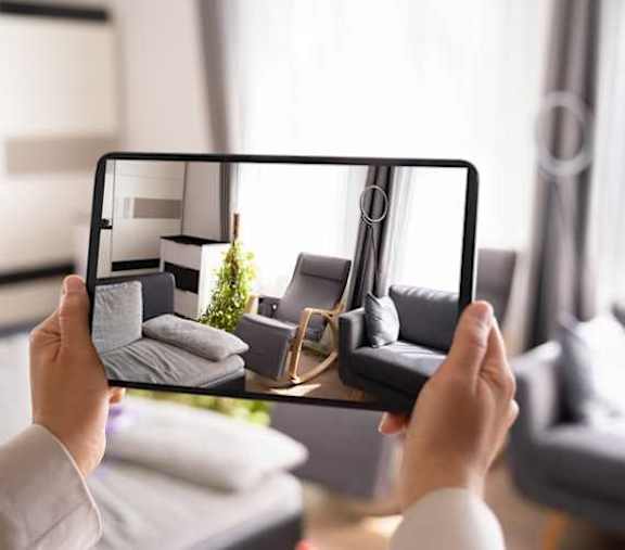 A person is holding a tablet with a photo of a living room on the screen.