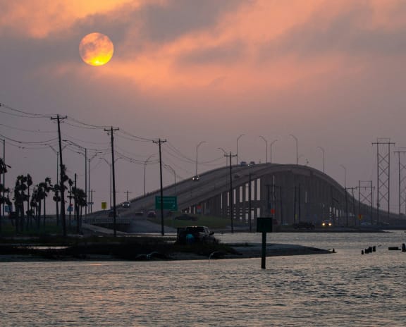 the sun sets over a bridge over the water and a body of water