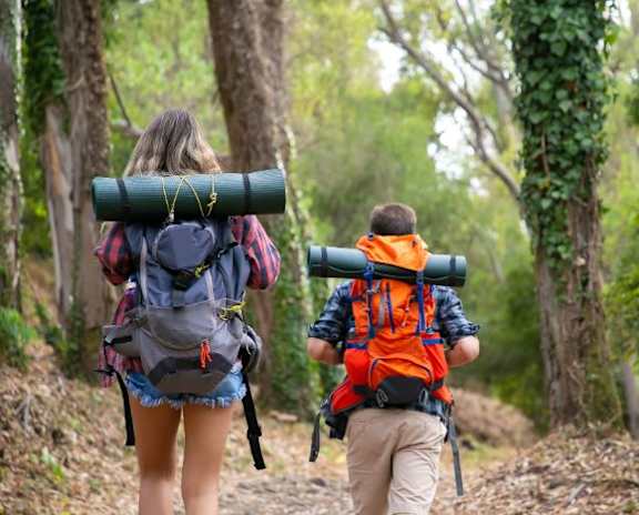 A man and a woman are hiking in the woods with a large green object on the woman's back.at The Robert Apartments, Alabama