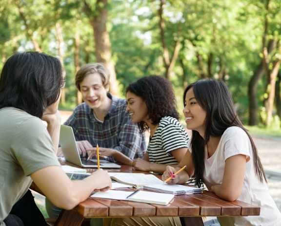 Four people studying outdoors at a picnic table.