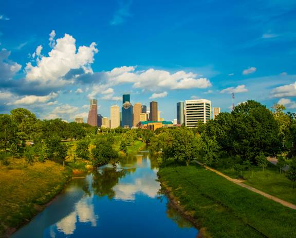 A river flows through a green landscape with a city skyline in the background.