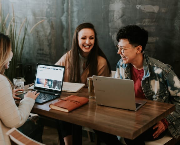 three people sitting at a table with laptops