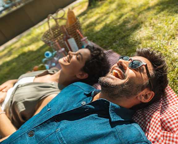 A man and woman are lying on a blanket in a park.