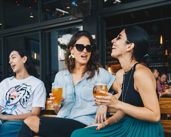 Three women are sitting on a bench, each holding a glass of beer.