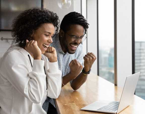 Two people celebrating in front of a laptop.