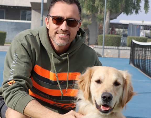 A man in a striped shirt holds a golden retriever.