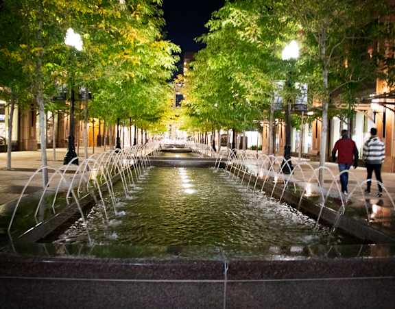 A fountain in the middle of a city street at night.