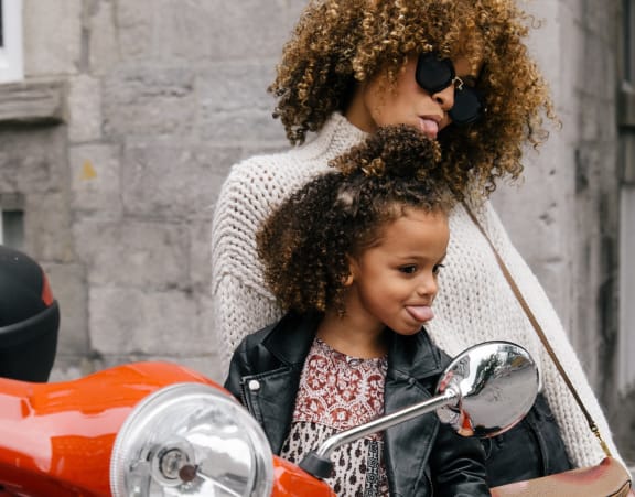 a woman and a young girl standing in front of a red motor scooter