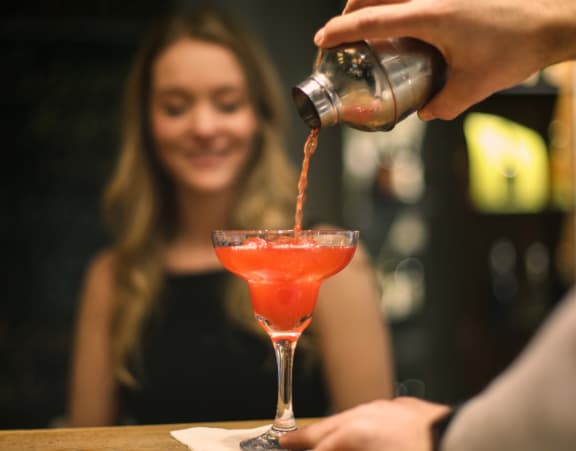 a bartender pours a cocktail into a glass