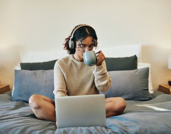 a woman sitting on her bed with a laptop and a cup of coffee royalty free adult stock at Topaz Apartments, Los Angeles, 90013