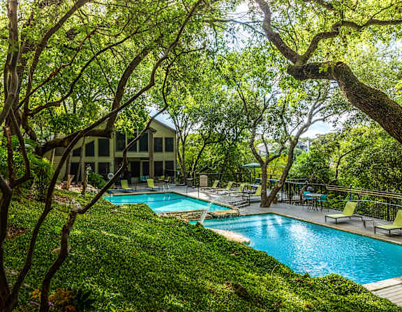 A pool surrounded by trees and a house in the background.