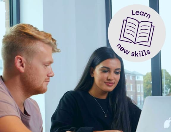 Two people are sitting at a table looking at a laptop screen.