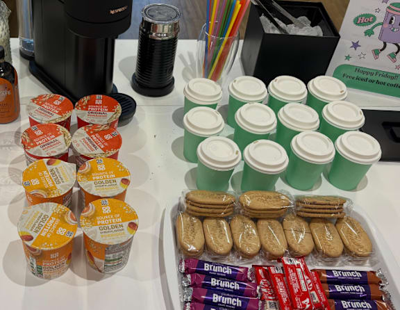 A woman is sitting behind a counter with a variety of snacks on it.