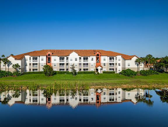 A large white building with a red roof is reflected in the water.