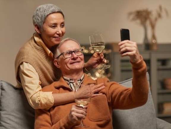an older couple enjoying their home, a glass of wine, and taking a selfie