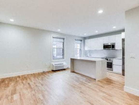 A spacious kitchen with a wooden floor and white walls.