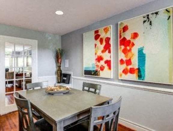 A dining room with a table and chairs and a painting on the wall.