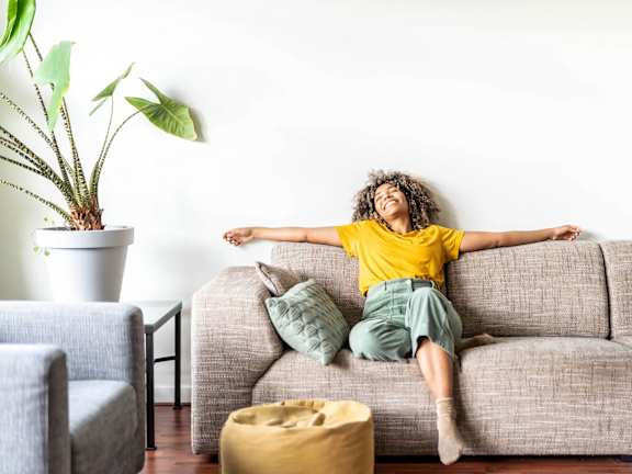A person in a yellow shirt is sitting on a grey couch with their arms outstretched.
