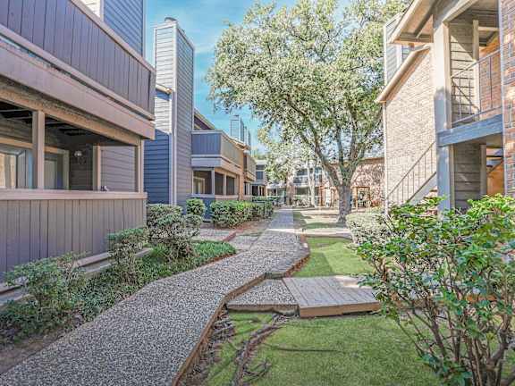 A gravel pathway leads through a landscaped area between two buildings.
