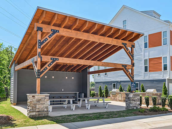 A wooden pavilion with a stone pillar and benches in front of a building.