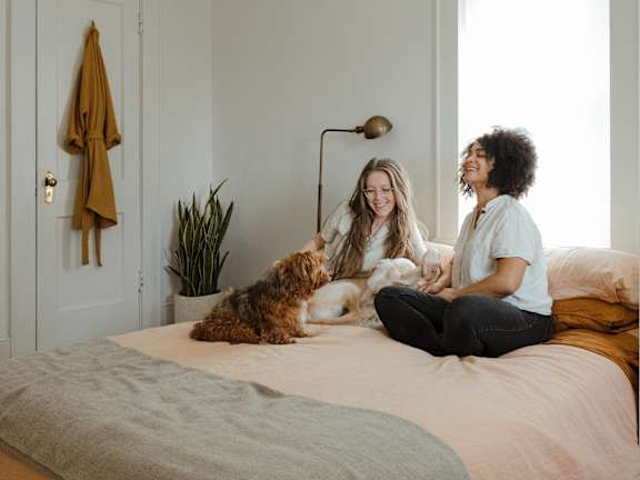 Two women sitting on a bed with a dog.