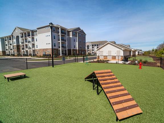 A long wooden bench sits on a green lawn in front of apartment buildings.