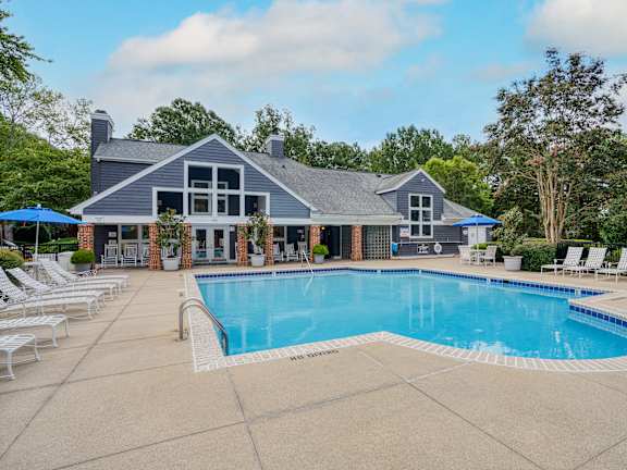 A large swimming pool in front of a house with a blue sky in the background.