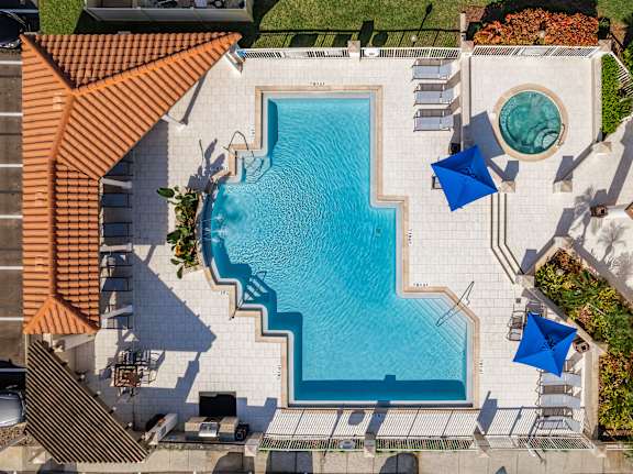 A swimming pool surrounded by a patio with chairs and umbrellas.