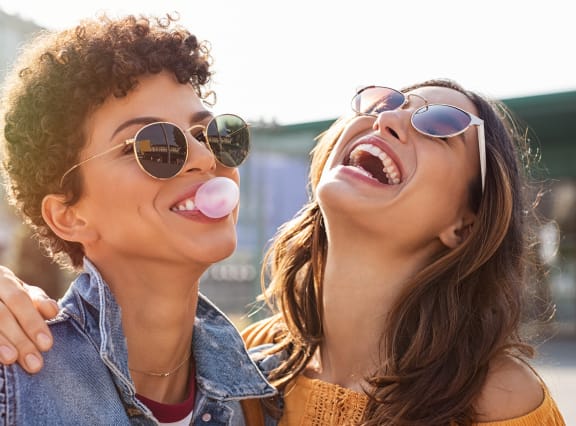 two women wearing sunglasses and laughing with their lollipops in their mouths in front of at Zeta Luxury Apartments in Sacramento, CA