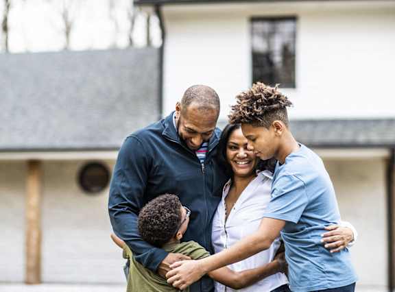 a family of four hugging in front of a house